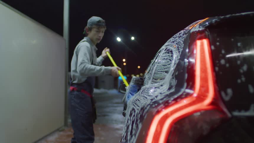 Man in cap cleaning the outside of a car with soap at night