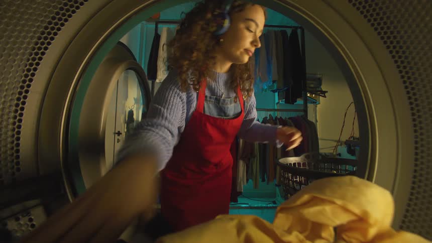 Woman in red apron and headphones putting clothes into a washing machine