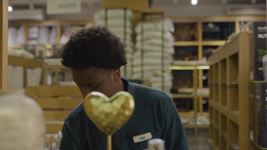 Young man placing decorative objects on a shelf in a store