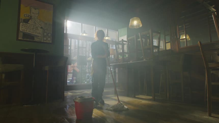 Woman cleans the floor of an empty bar with chairs stacked up