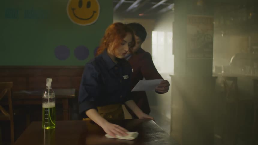 A woman takes a wooden stool off a table and starts cleaning it and then a man comes and hands her a letter