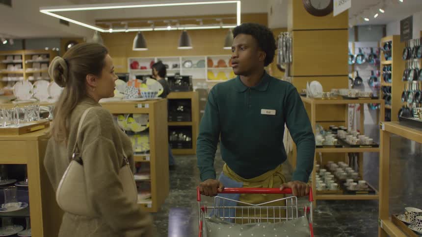 Clerk walking with a shopping cart through a store with customers