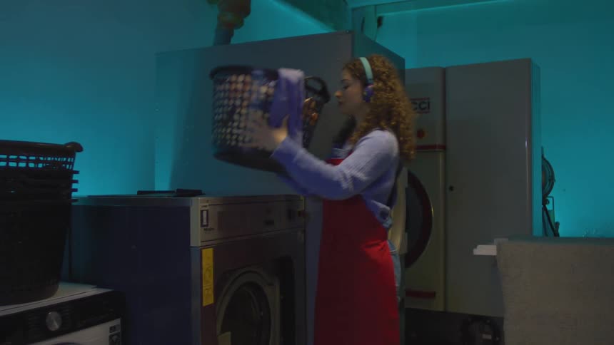 Woman with headphones taking clothes out of a washing machine and putting them in a basket