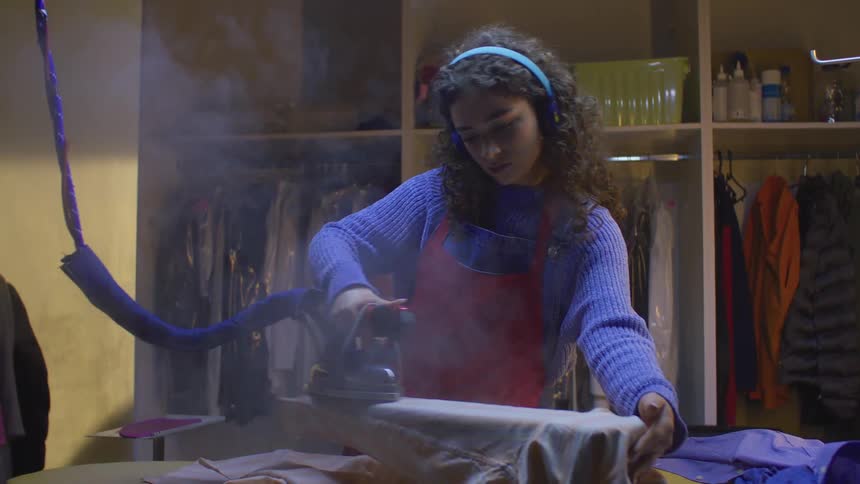 Two women in an indoor space ironing clothes with an industrial iron