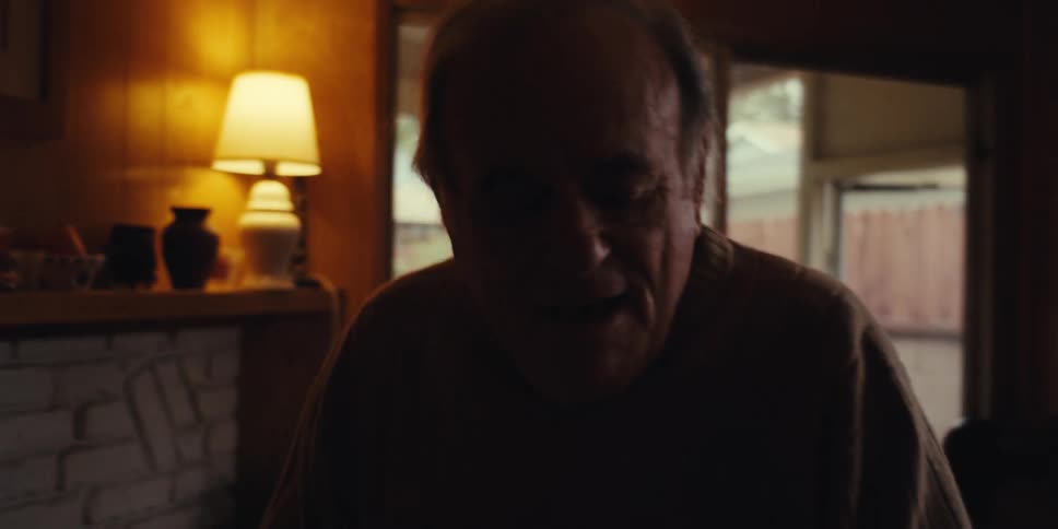 An elderly man is dancing alone while cleaning a dimly lit room at home
