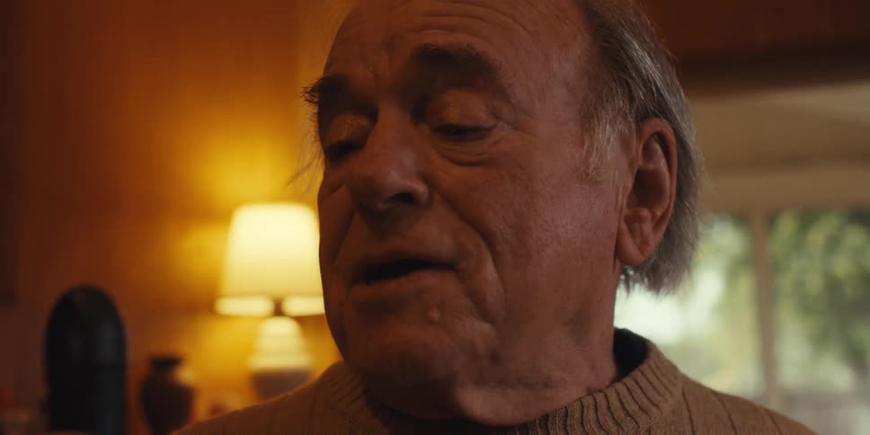 An elderly man sings into the handle of a broom in a cozy room at home
