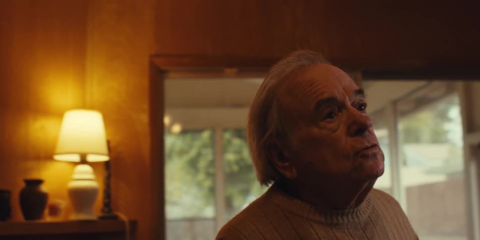An elderly person sings while using a blue dust mop to clean a wooden floor at home