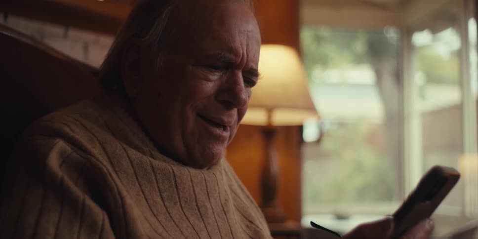 Portrait of an elderly man sitting in an armchair looking incredulously at his cell phone