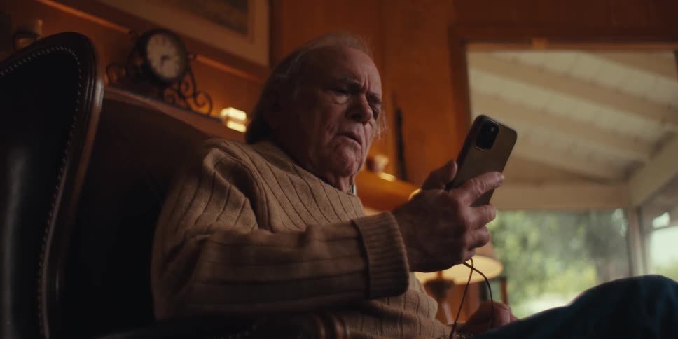 Elderly man sitting in a leather armchair getting shocked while sitting and interacting with a smartphone