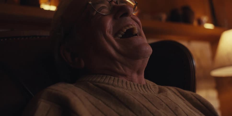Elderly man with glasses sitting in a dark leather armchair smiling while interacting with a smartphone