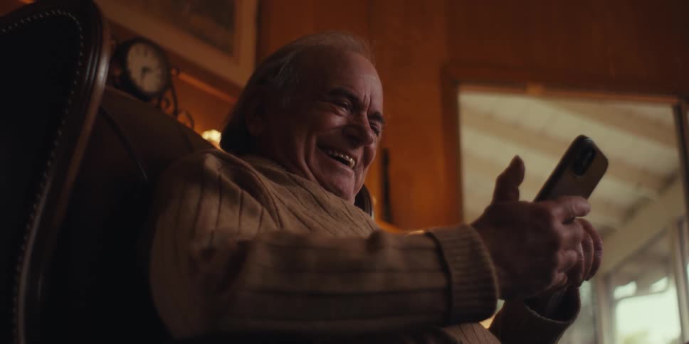 Elderly man sitting in an armchair laughing and interacting with his cell phone