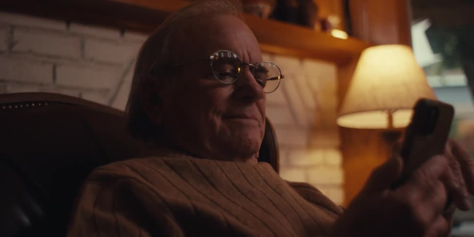 Happy elderly man sitting in an armchair and interacting with his cell phone