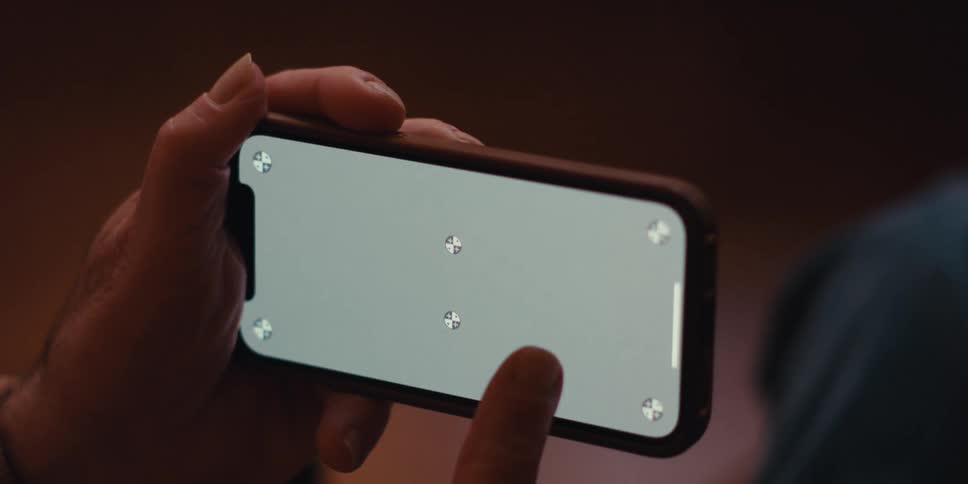 A person is holding a smartphone horizontally with both hands displaying a screen with four crosshair symbols at the corners and a central rectangular area