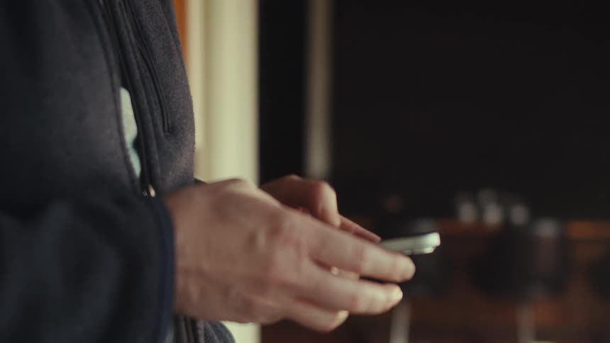 Man stands indoors texting on a smartphone