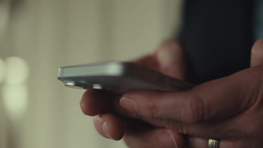 A mans hands one of which wears a ring use a silver smartphone