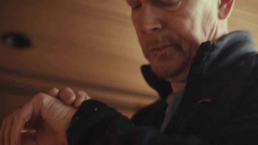 A middle aged man in a dark jacket checks his watch