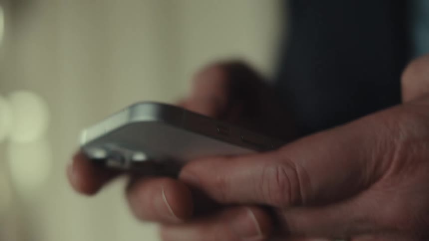 Man wearing a ring and a black jacket uses a silver smartphone
