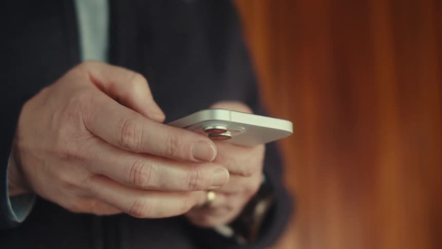 Closeup of a man handling a silver smartphone in a room