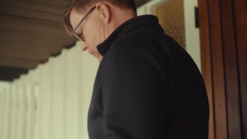 Middle aged man wearing glasses and a black jacket holds a light colored package