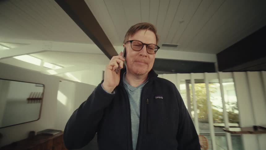 A man talks on a smartphone while walking inside a luxurious modern house