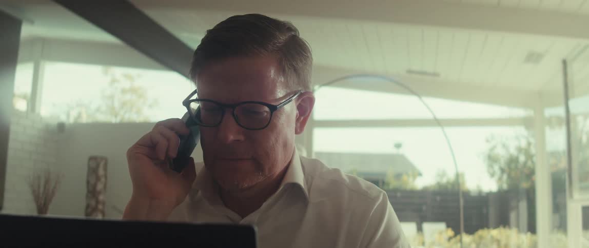 Man in glasses and a white shirt interacts with a laptop and a smartphone