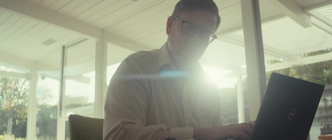 Man in glasses and a white shirt works at a desk with an open laptop