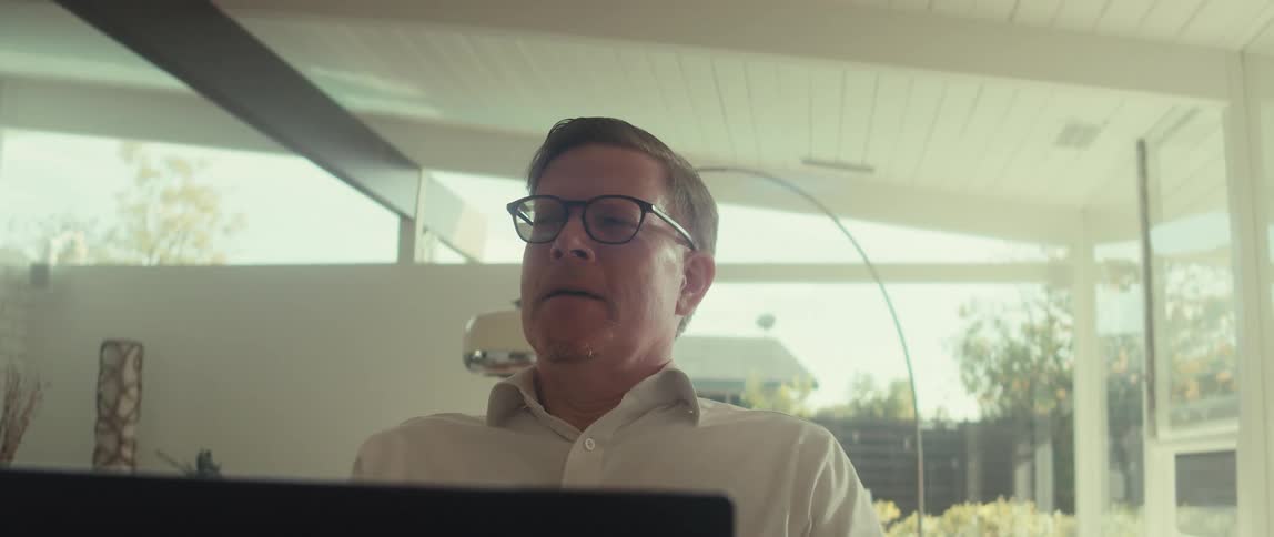 Man in glasses and a white shirt is sitting in front of a laptop
