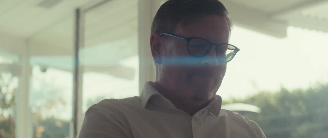 Man wearing glasses and a white shirt sitting in a room lit by natural light