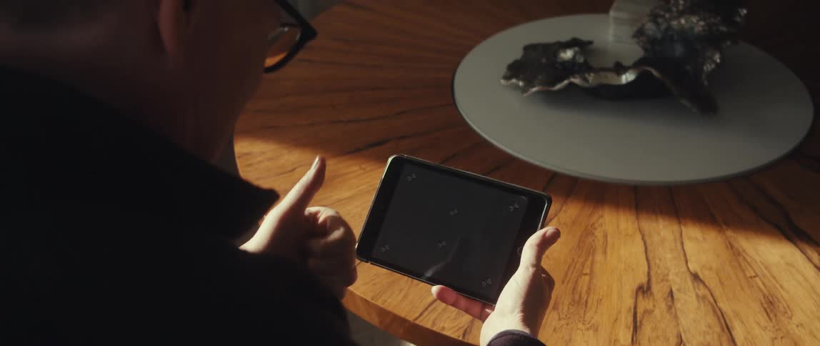 A person holds an ipad mini displaying a test pattern speaking into it while seated at a coffee table with a white and silver centerpiece