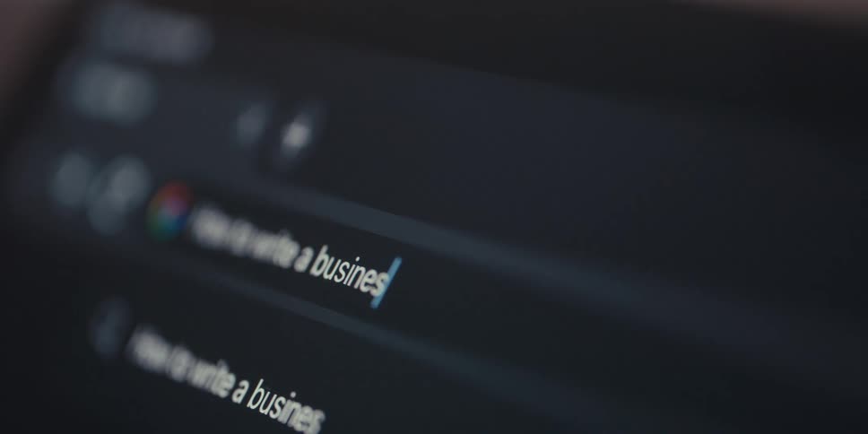 A user types how to write a business plan into a laptops google chrome search bar with the text briefly going out of focus as new words are added before transitioning to the results page