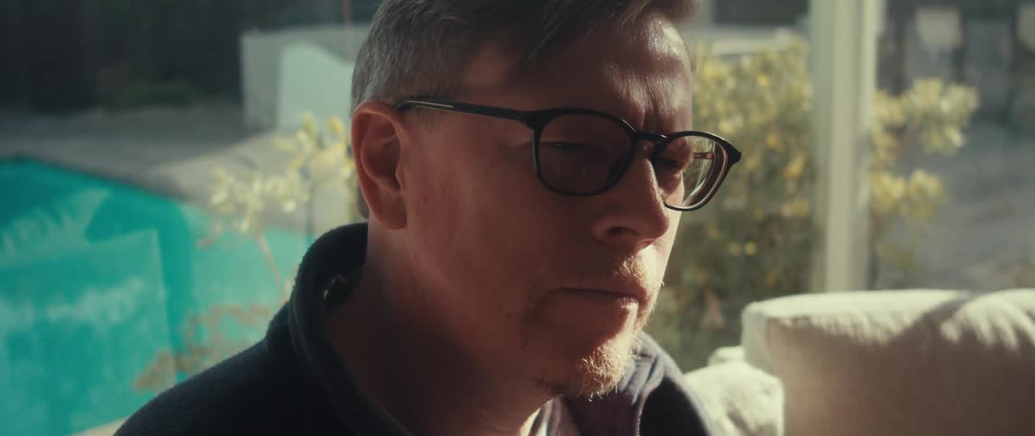 A man with glasses looks down at and operates a tablet device