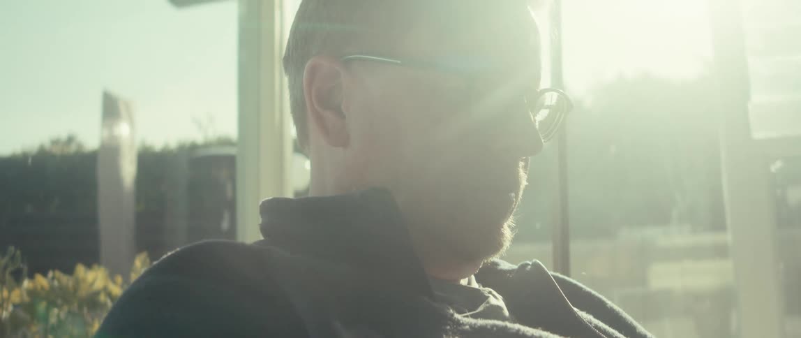 A man with glasses sits on a couch and interacts with his smartphone in a bright room