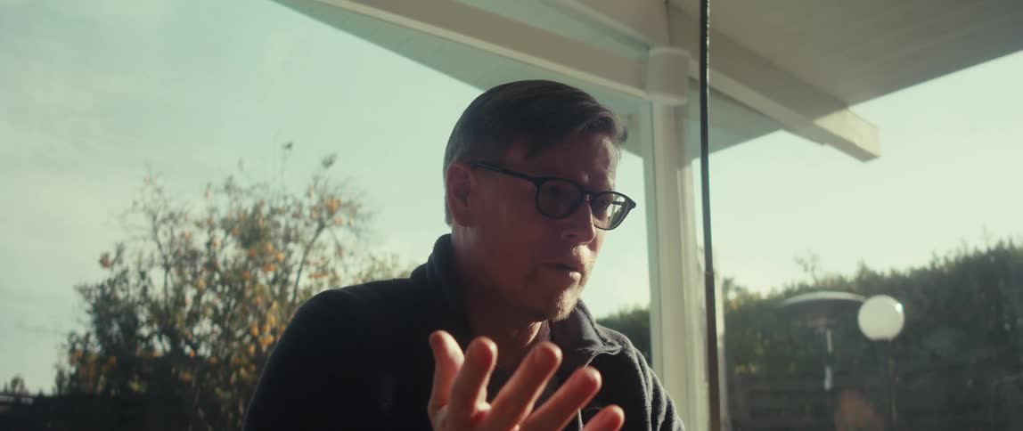 The face of a mature man wearing glasses and speaking to you while gesturing with his hands