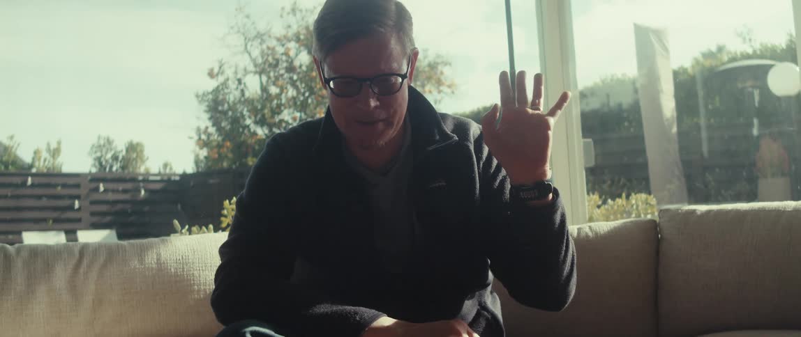 Man sitting on a sofa waves his hand while looking at a tablet on the table