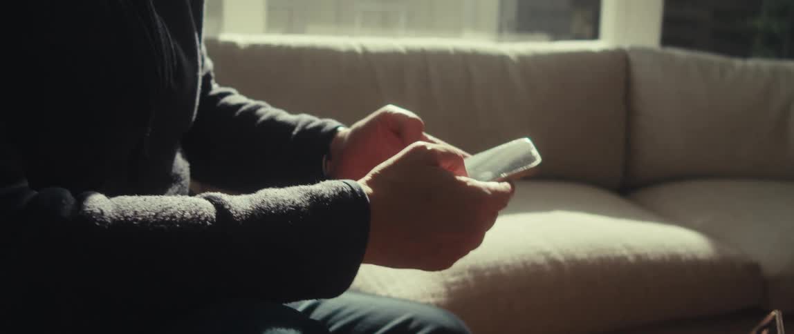 Man holds a smartphone reflecting sunlight while sitting on a sofa
