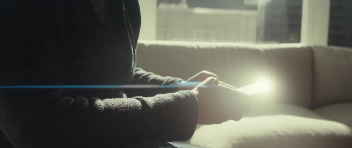 A person in glasses using their phone while sitting on a couch in a bright room