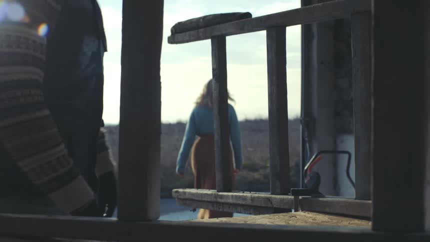 A man working on a ladder in a dilapidated building is approached by a woman outside