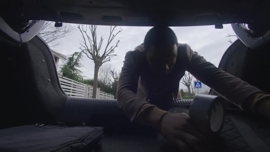 Man putting a backpack in the trunk and picking up a black garbage bag