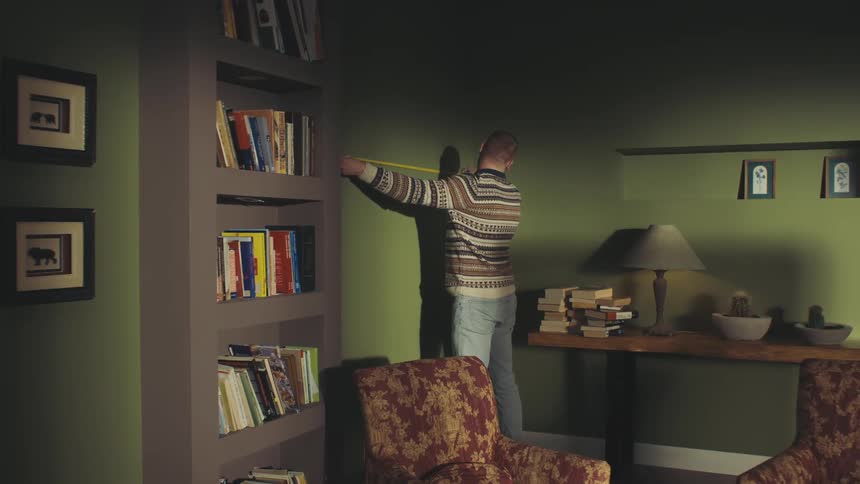 A person in a patterned sweater is measuring the walls in a cozy modern room with green walls