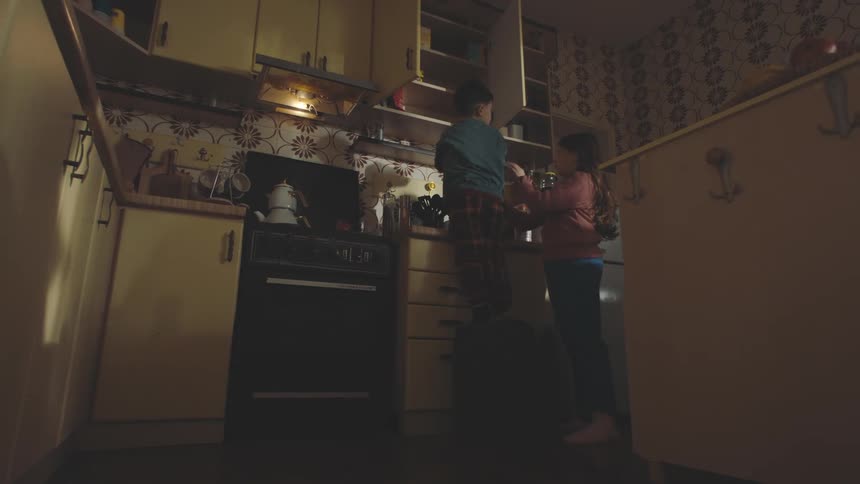 Boy climbing on a stool and picking up a cookie jar and handing it to another girl