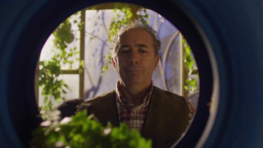 Man decorating a blue tire suspended on ropes with green plants
