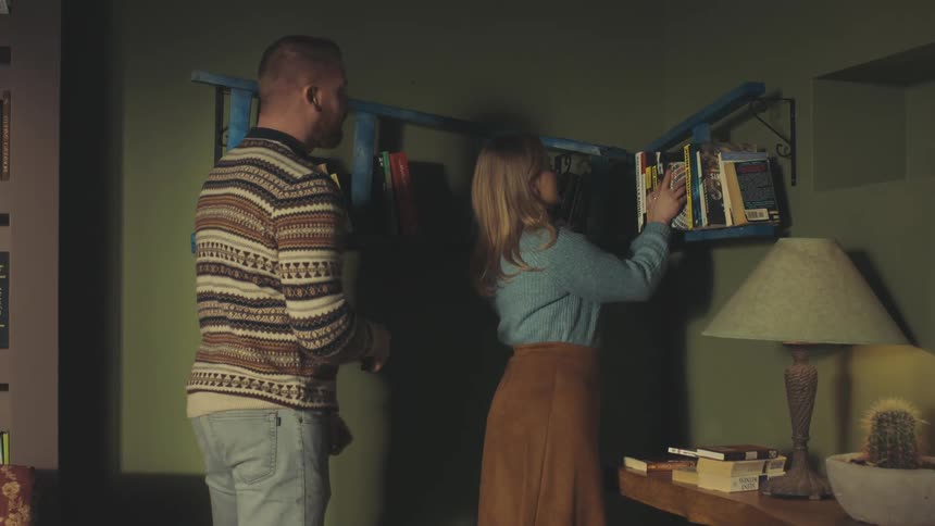 Man and a woman placing books in an organized manner on a ladder taped to a wall