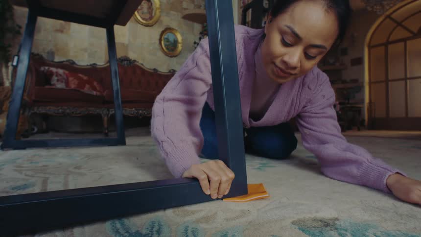 Woman placing an orange sponge beneath the leg of a table