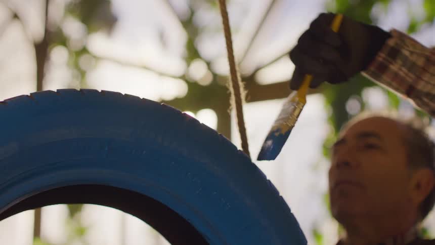 Man uses a small brush to paint the tire of a tire swing blue