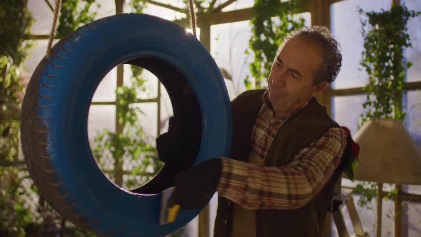 A man is painting a hanging tire blue