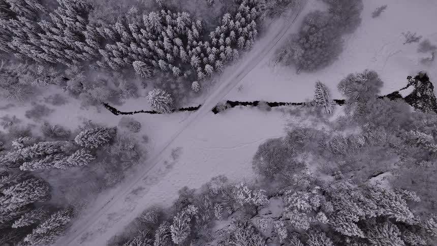 Birds eye view of a small creek running under a road in snow covered forest