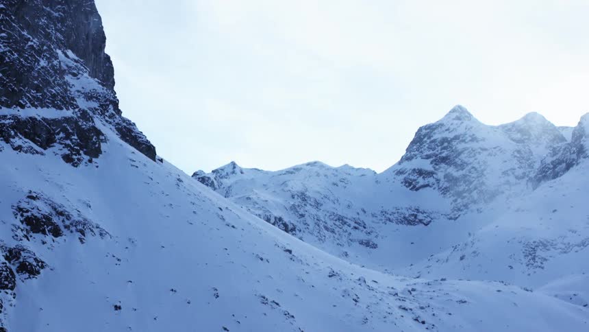 Snow covered mountain peaks rise above a layer of fog under a clear blue sky