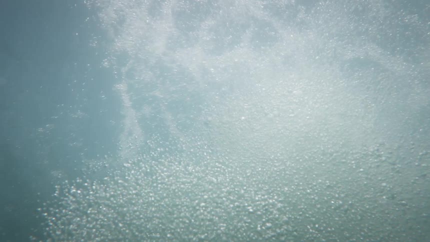 A person jumping into the water creates a trail of air bubbles rising upward underwater