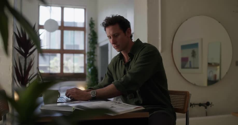 Man typing on a laptop and using a book next to it