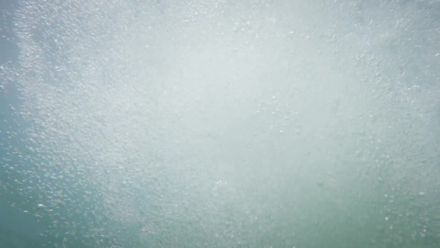 A person jumping into the water creates a trail of air bubbles rising upward underwater